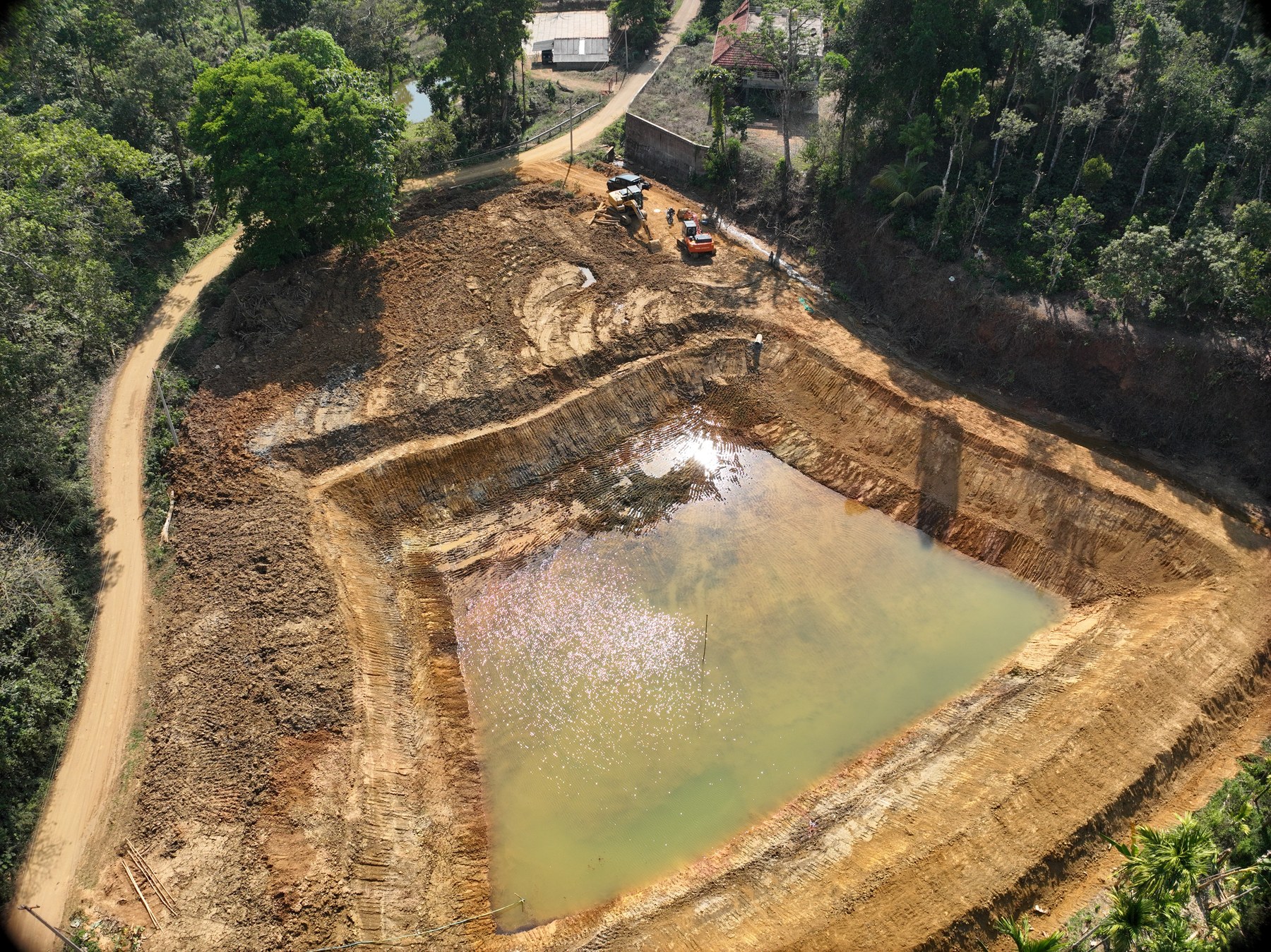 Oblique drone photo of a farm pond under construction, partially filled with water, excavator visible at the edge