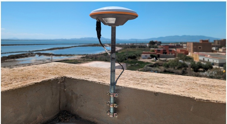 RTK GNSS antenna mounted to a rooftop parapet, cabled down to a correction radio